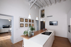 ONLINE 12/9/2022                        ADOBE STOCK 530752631      :         ENVATO                                          : SHUTTERSTOCK 2200709487 :                          PROGETTO BIANCHI-BOSONI ARCH.         View of a modern white kitchen, in the foreground, is the island kitchen with induction hob, the floor and the ceiling are made of wood