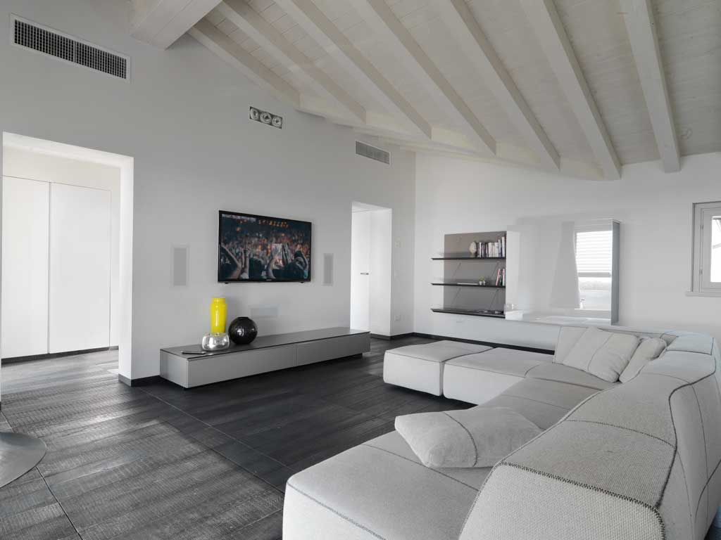 Attico a Mantova presso la Corte Benedetta, moderno soggiorno con pavimento in parquet di Listone Giordano, in primo il grande divano in tessuto grigio