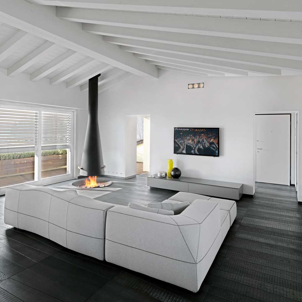 Vista interna del soggiorno con camino  a sospensione in metallo verniciato e un divano in tessuto grigio, pavimento in parquet modello Medoc di Listone Giordano