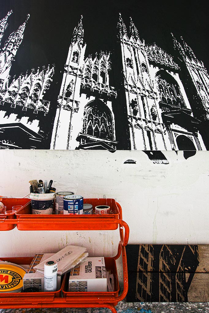 Carrello con barattoli di vernice sotto ad un opera raffigurante il Duomo di Milano