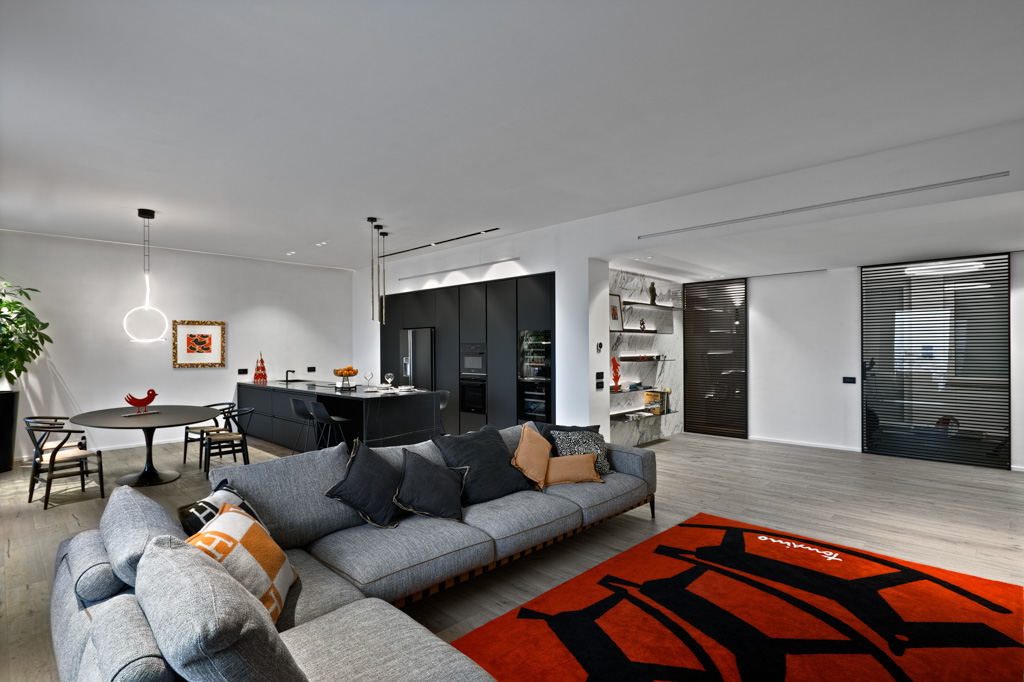 This modern living room features a red carpet and a fabric sofa, with an open-plan kitchen and dining area in the background